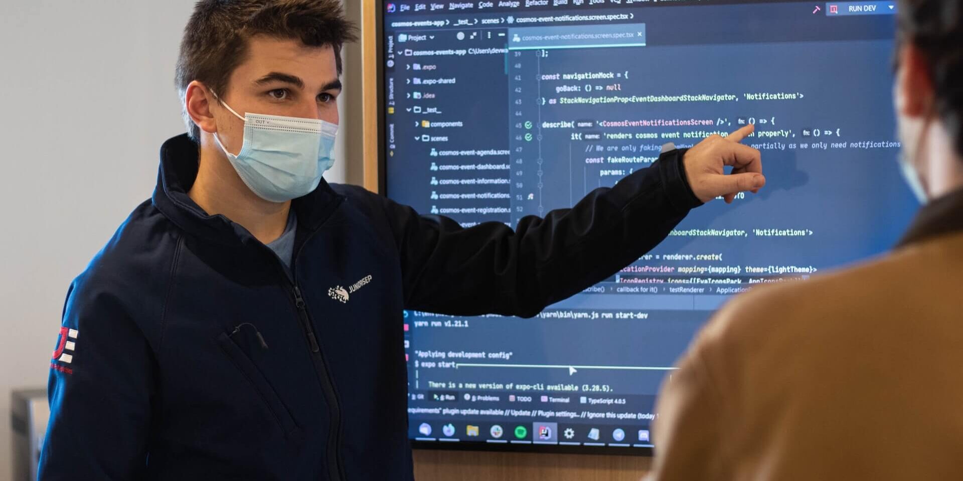 IBKyH0V3rew Two people working, and discussing about a presentation with code on a screen. Student showing code on a tv.