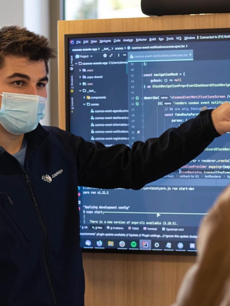 IBKyH0V3rew Two people working, and discussing about a presentation with code on a screen. Student showing code on a tv.